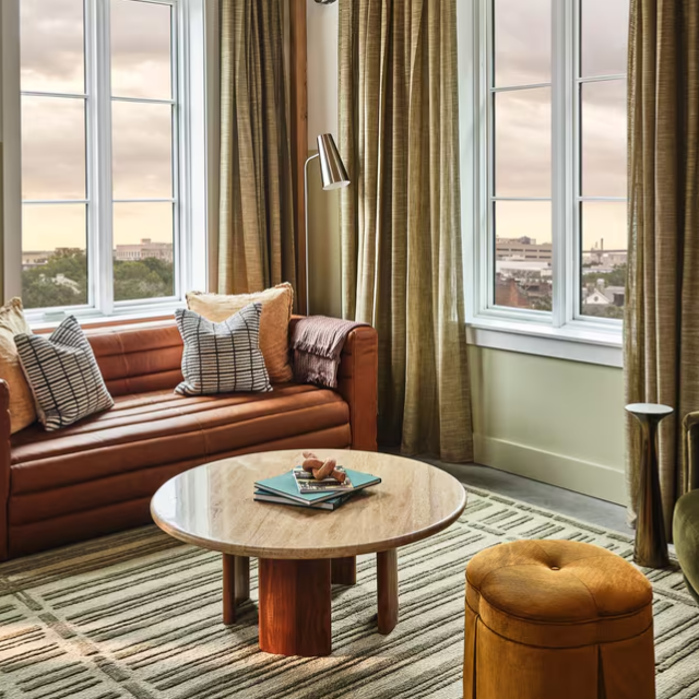 A hotel room suite living room with seating, coffee table and large windows.