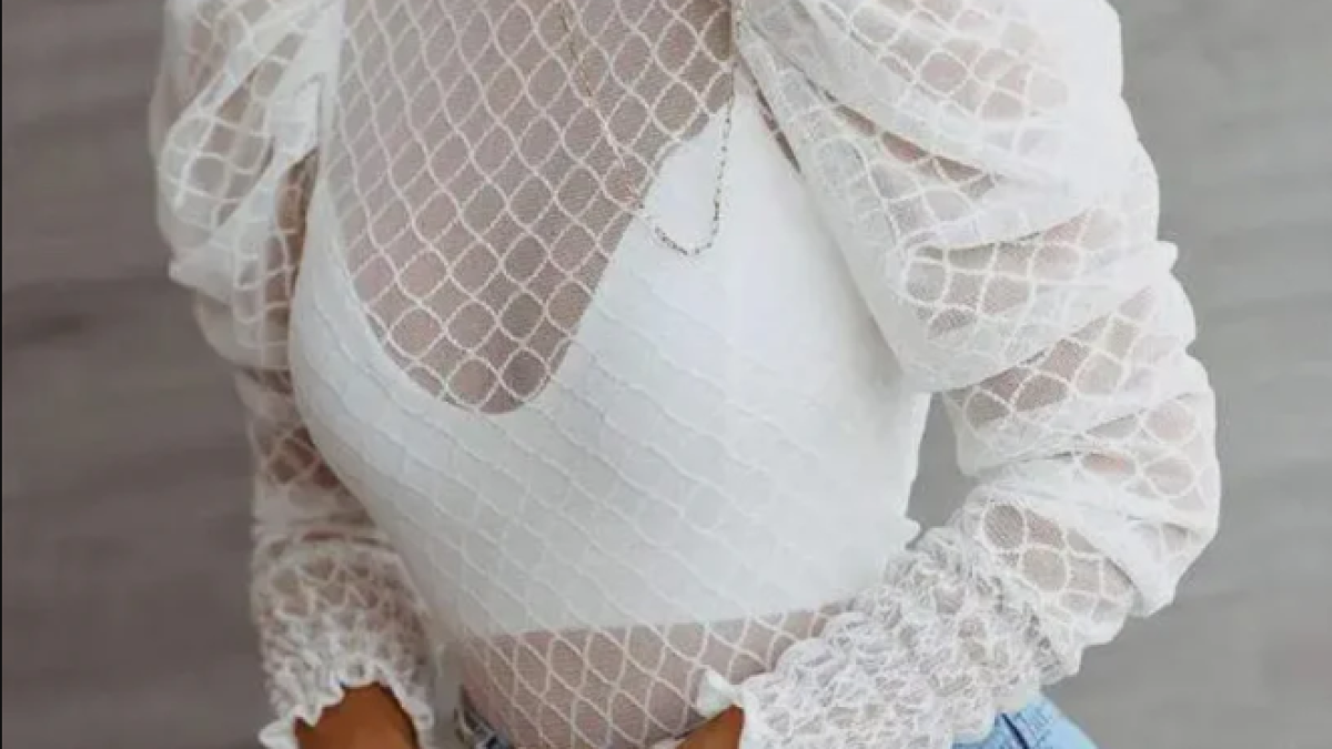A model posing in a white see-through blouse and gold accessories.
