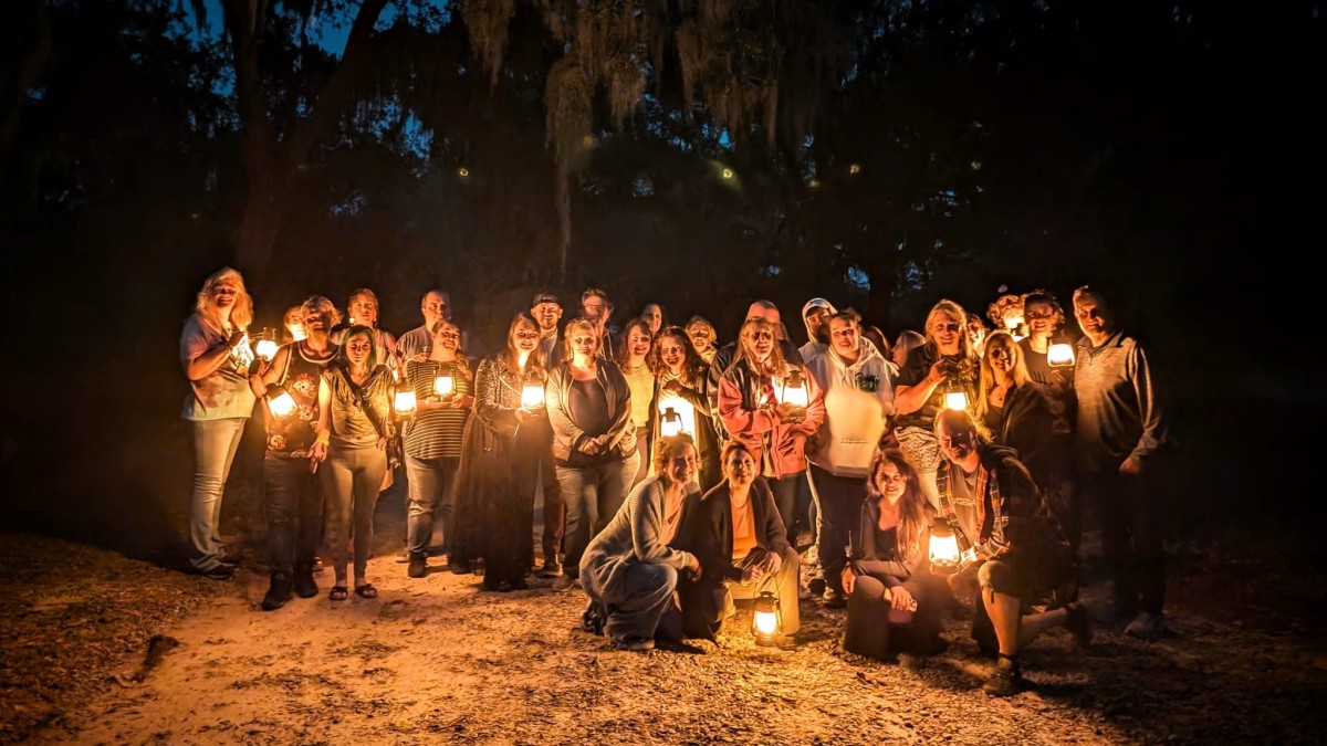 A large group of people in the dark holding lanterns on a ghost tour.