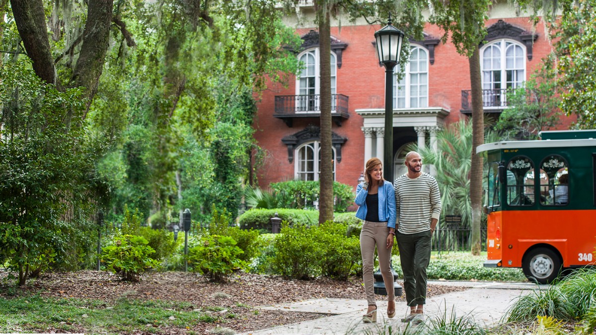 A couple strolls in Monterey Square in front of the Mercer Williams House in Savannah